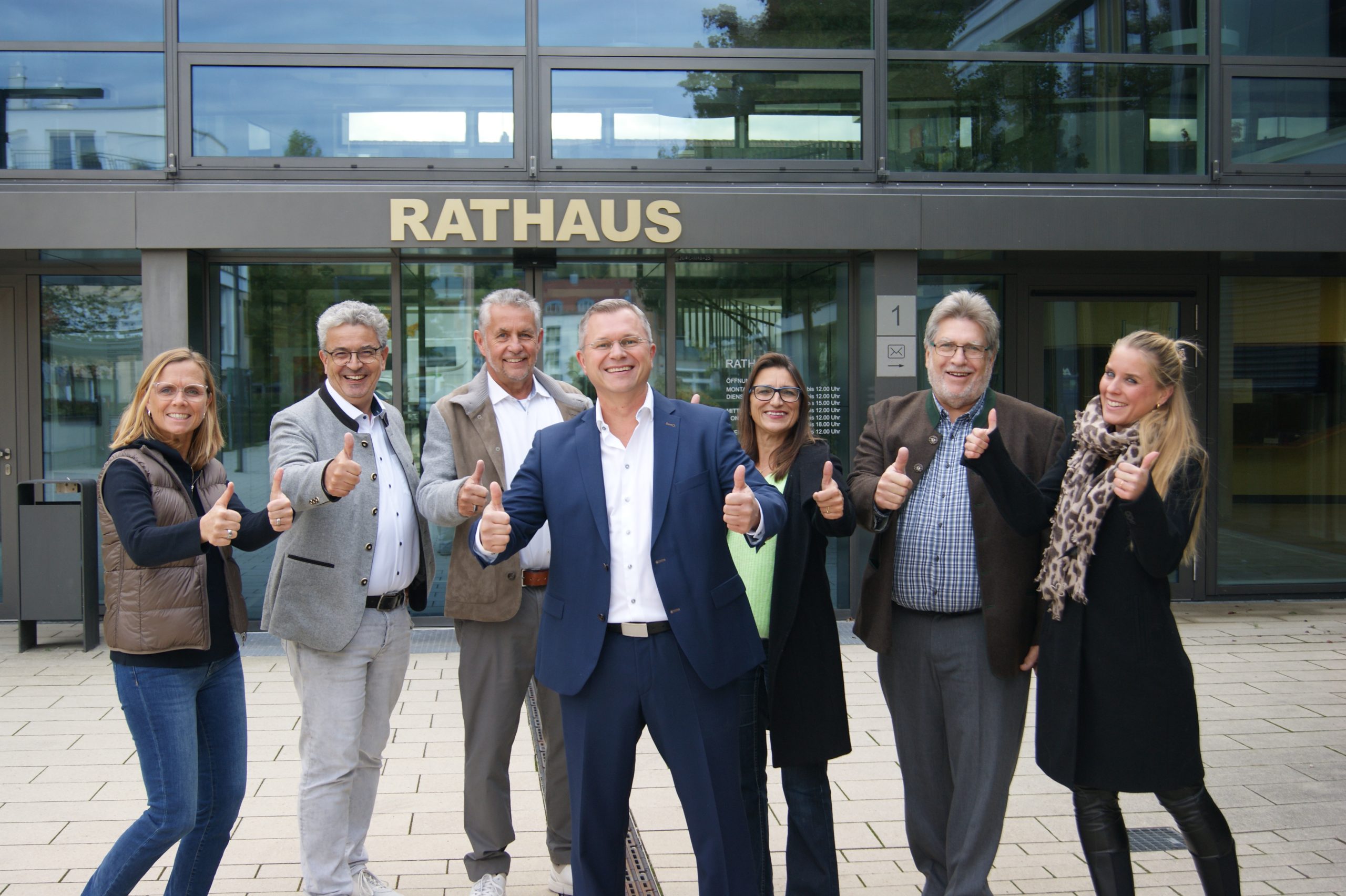 Die Parteimitglieder der Freien Wähler Gilching stehen lächelnd vor dem Rathaus und zeigen die Daumen nach oben.