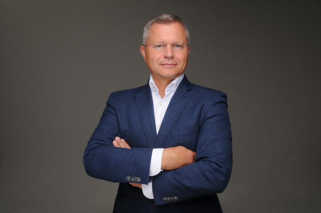 Stefan Siegl, kandidierender Bürgermeister der Gemeinde Gilching, im Porträt im dunkelblauen Anzug mit verschränkten Armen vor dunklem Hintergrund.